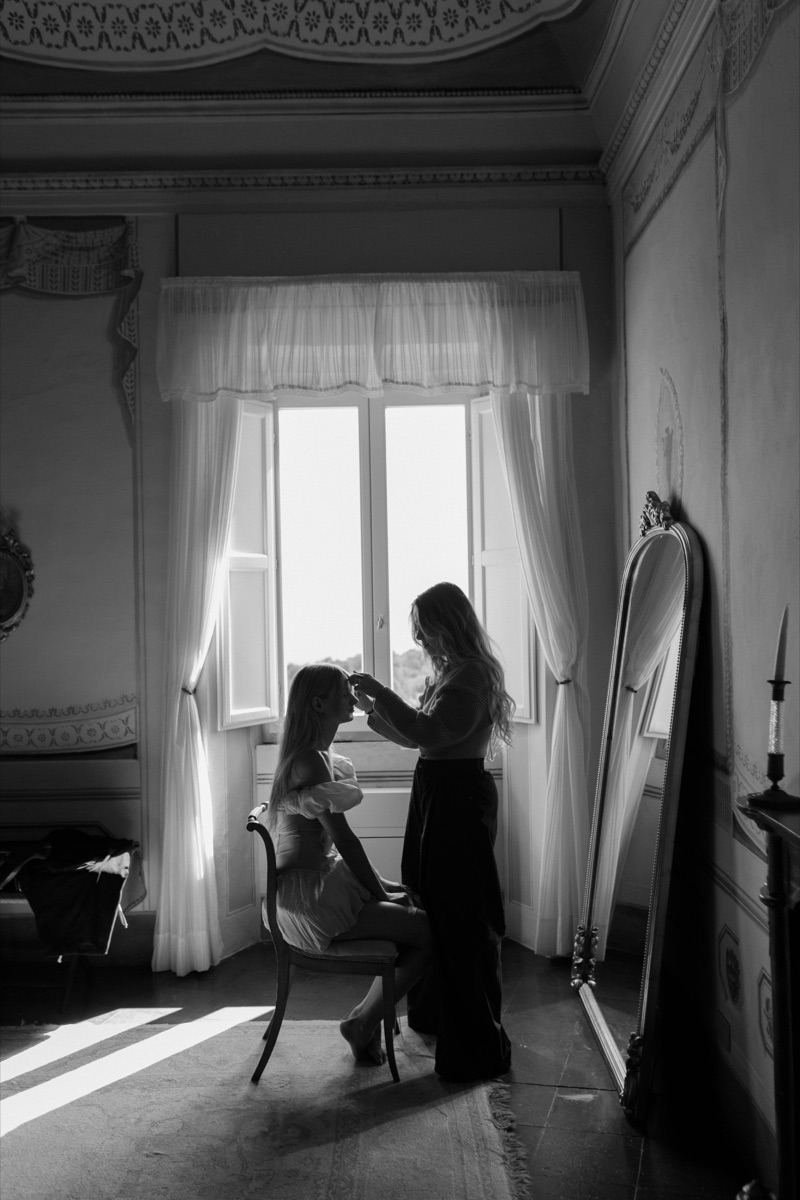 Mariée coiffée à contre-jour devant une fenêtre, photo en noir et blanc