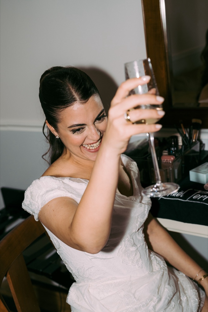 Mariée souriante, coiffure relevée et maquillage terminé, verre à la main